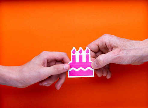 Illustration de fête, pictogramme imprimé de gâteau avec bougies rose tenu par deux mains en opposition, sur fond orange. Amusement, déchirement