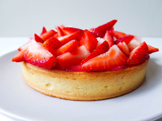 Modern french dessert. Strawberry tart: crunchy pâte sablée dough, almond frangipane, strawberry coulis and fresh strawberries for decoration. Tart is on a light plate. White background.  Back view.