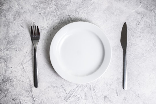 Empty white plate with cutlery on a gray background.
