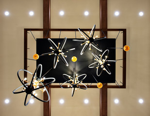 a modern styled handelier hanging from wooden beams on a white ceiling