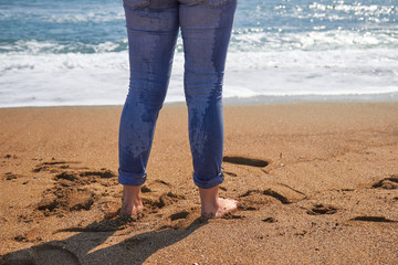 Girl in blue jeans standing on sand at the beach. Vacation travel lifestyle photo. Young beautiful woman near the sea or ocean.