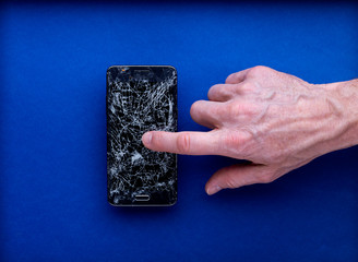 Smartphone écran cassé brisé isolé sur fond bleu avec main qui pointe doigt sur l'écran
