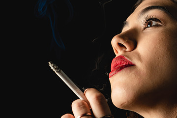 Obraz premium Low key close-up young woman smoking cigarette on black background. Copy space for text message.