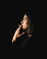 Low key close-up young woman smoking cigarette on black background. Copy space for text message.