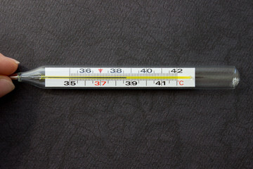 Mercury thermometer in hand on black background. Close up photo. Thermometer shows a temperature of 38.7 degrees Celsius
