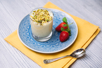 Pistachio parfait in a transparent glass cup on a blue plate with two strawberries, on a yellow napkin with a teaspoon.