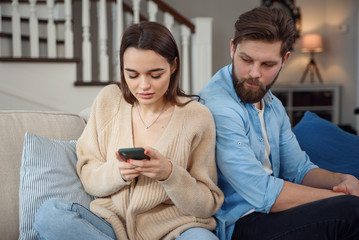 Modern couple at home. Man and woman concentrated on messaging with smartphones, ignoring each other and spending time on social media.