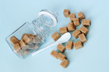 Brown cane refined sugar in a jar and white spoon on light blue background.