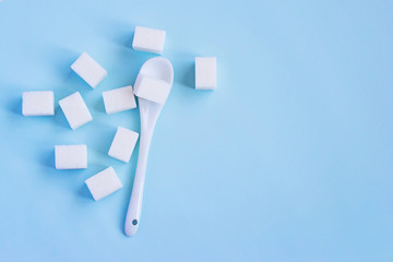 White refined sugar and spoon on light blue background. Top view with copy space.