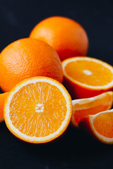 Halves and slices of fresh juicy oranges on black textured background.