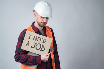 I need a job.Builder is looking for work. Concept - dismissal workers building. Sad guy with a sign in his hands. Inscription need a job on cardboard. Concept - layoffs due to closure of construction