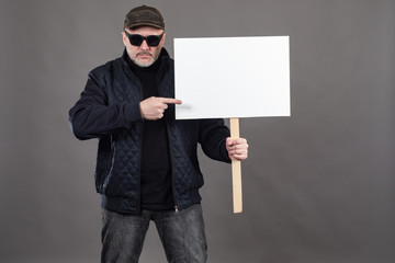 Adult man holds a banner. Human in a cap and eyes protests. Man shows a finger on a white banner....