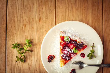 Beautiful traditional italian cheesecake with red fruits, mint, and powdered sugar on wooden background, selective focus.