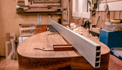 closeup scene of a precision process for building a stringed musical instrument, checking neck angle with a straight edge