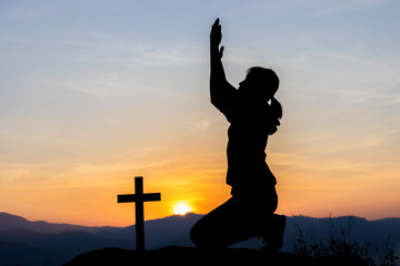 Silhouette of human kneeling down praying to the God at sunset background. Christian, Christianity, Religion copy space background.