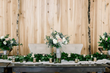 Fototapeta na wymiar Head Table at a Rustic Wedding decorated with bridal bouquets in clear vases and a beautiful green garland accented with blush and white roses and candle votives. 