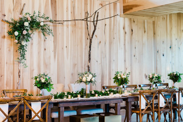 The Head Table at a Wedding Reception in a Barn, Decorated with Rose and Green Wedding and Bridal Bouquets in Glass Vases. The Table is Decorated with Green Leaves. 