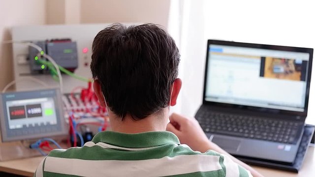 Back View of Young Man Who is Working Home Office and Making Online Education about PLC and Operator Panel Programming. Distance learning, also called distance education, e-learning or online learning