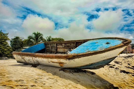 Old paint shedding boat sits on crest of sand mound with palm trees in the background. 