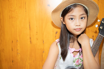 A portrait of a cute Asian elementary school girl with a ukulele, a popular musical instrument for...
