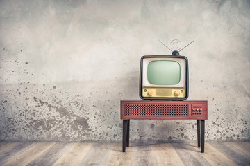 Old retro classic analog CRT TV set receiver and aged wooden television stand with outdated amplifier front aged concrete wall background. Broadcasting, news concept. Vintage style filtered photo
