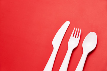 Plasic white cutlery set with red background. Top view