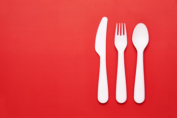 Plasic white cutlery set with red background. Top view