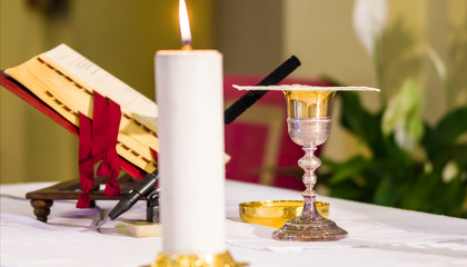 Naklejka na ściany i meble lit candle illuminates chalice with wine and ciborium with the host, ready for the communion of the faithful