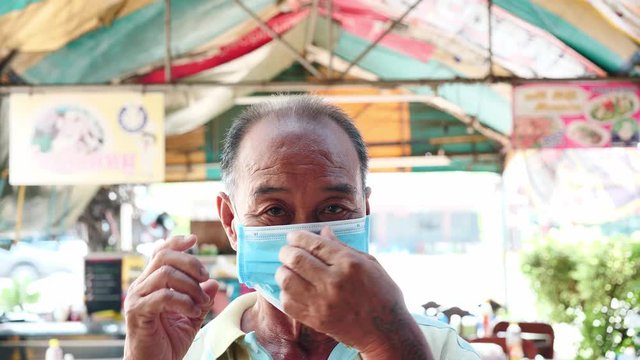 Close Up Face Of Asian Elderly Man Wearing Mask Protect Viruses Coronavirus (COVID-19) Outbreak Prevention On Restaurant Background. Health Care And Protection Concept.