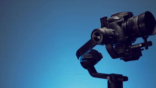 Estabilizador o Gimbal con una camara montada, haciendo movimientos de grabacion con fondo de color azul