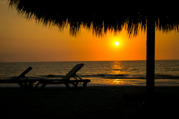 Playa con palapa y camastros mientras el sol se pone debajo del mar