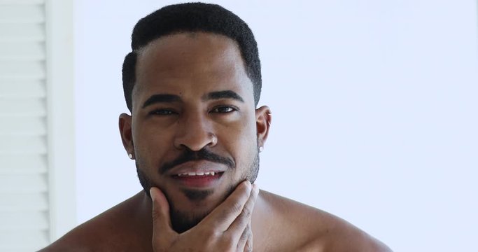 Confident attractive young adult shirtless sexy african hipster man enjoying new haircut and beard grooming looking at camera. Male self care, anti-dandruff shampoo and barbershop services concept.