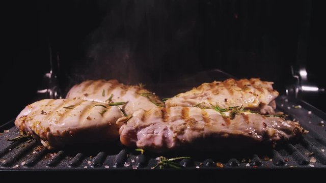 Delicious juicy meat steak cooking on the grill. Cook grilling fresh chicken breast. Fry chicken fillet on electric roaster. Pour salt, rosemary, black pepper. Slow motion.