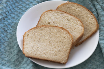 Sliced of freshly, homemade white bread on a white plate with a textured blue cloth background.