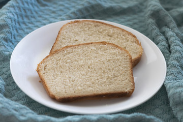 Sliced of freshly, homemade white bread on a white plate with a textured blue cloth background.