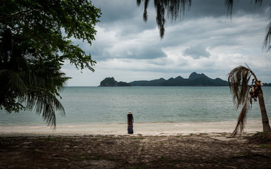 woman in white fedora hat and sarong standing on the beach with islands in the background
