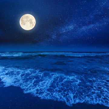 beach and sea on a cloudy night. beautiful view of waves rolling the coast beneath a glowing sky in full moon light