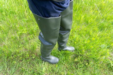 fisherman stands in rubber boots for a swamp in the river and holds a fishing rod in his hand in the summer