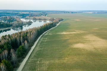 aerial view of country road between green fields and blue lake. rural landscape