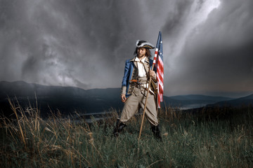 Man in United States War of Independence soldier costume with flag posing in forest. 4th July...