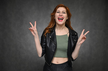 Portrait of a young pretty woman with beautiful hair and excellent make-up in a green T-shirt and a black jacket on a gray background. The model shows different emotions by changing poses.