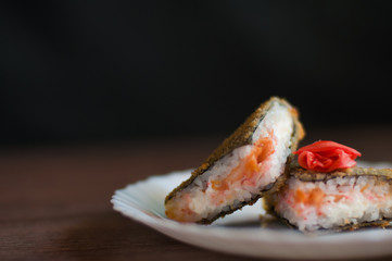 Fried sushi served on a white plate with cream cheese, salmon, and ginger, on a dark background. Side view. Japanese food.