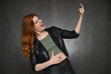 Portrait of a young pretty woman with beautiful hair and excellent make-up in a green T-shirt and a black jacket on a gray background. The girl demonstrates vivid emotions by changing poses.