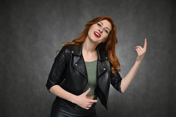 The girl demonstrates vivid emotions by changing poses. Portrait of a young pretty woman with beautiful hair and excellent make-up in a green T-shirt and a black jacket on a gray background.