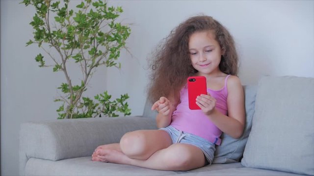 Curious cute boy preschool child using a digital tablet technology device looks telephone.Plays in the phone sitting on the sofa alone.Children tech addiction concept play game at home.