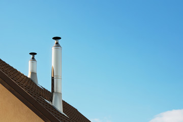Two modern style chimneys from oven and fireplace stacked stainless steel on tiled roof made according to fire safety requirements and to avoid condensation when reaching dew point in flue gases.
