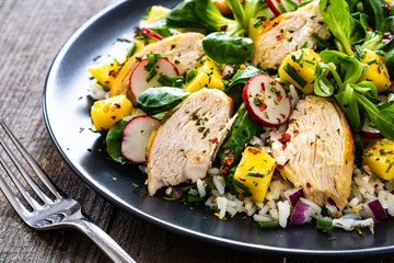 Caesar salad - fried chicken breast, white rice and vegetables on wooden table

