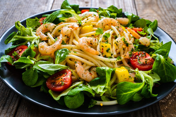 Spaghetti with prawns and vegetables on wooden background