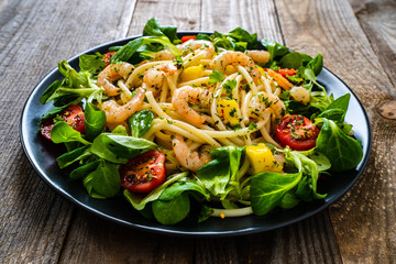 Spaghetti with prawns and vegetables on wooden background