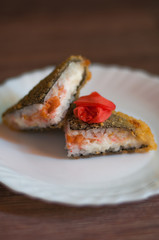 Fried sushi on a white plate with cream cheese, salmon, and ginger on wooden background. Side view. Japanese food.